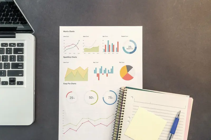 Laptop beside printed marketing charts and a notebook