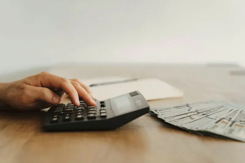 A hand working a calculator beside stacks of banknotes