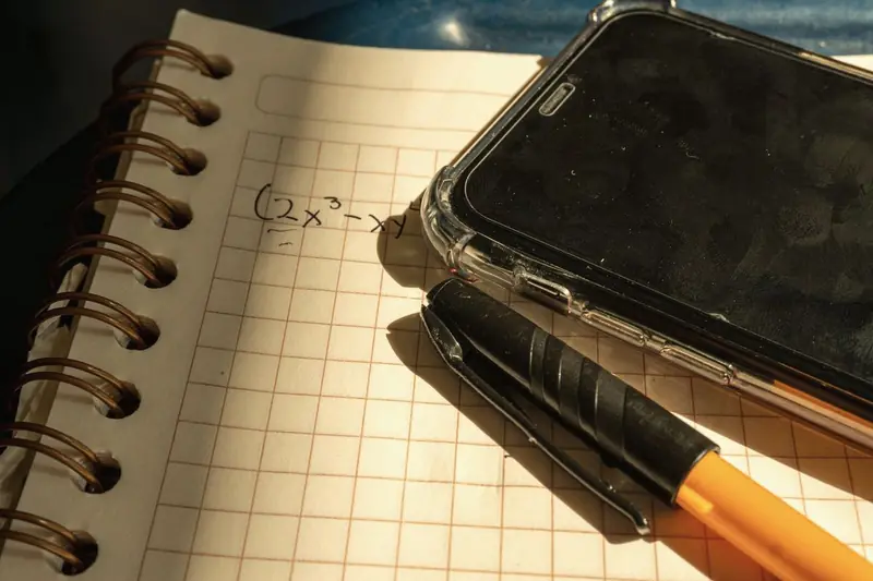 Notebook with an equation on squared paper beside a phone