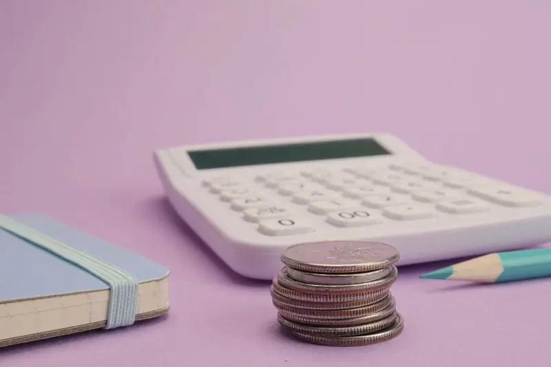 Calculator, stacked coins and a pencil on a purple desk