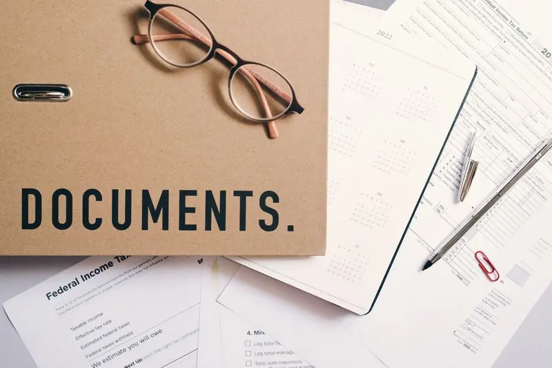 A documents folder, reading glasses and papers on a desk